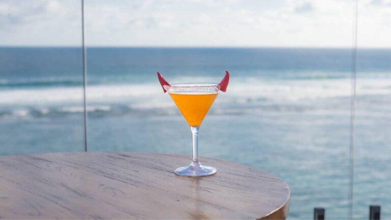 Devilʼs Flame cocktail at Klive Beach Club Uluwatu — bright orange Halloween drink with red devil horn garnish overlooking the Bali ocean during Haunted by the Sea & Tropical Mischief 2025.