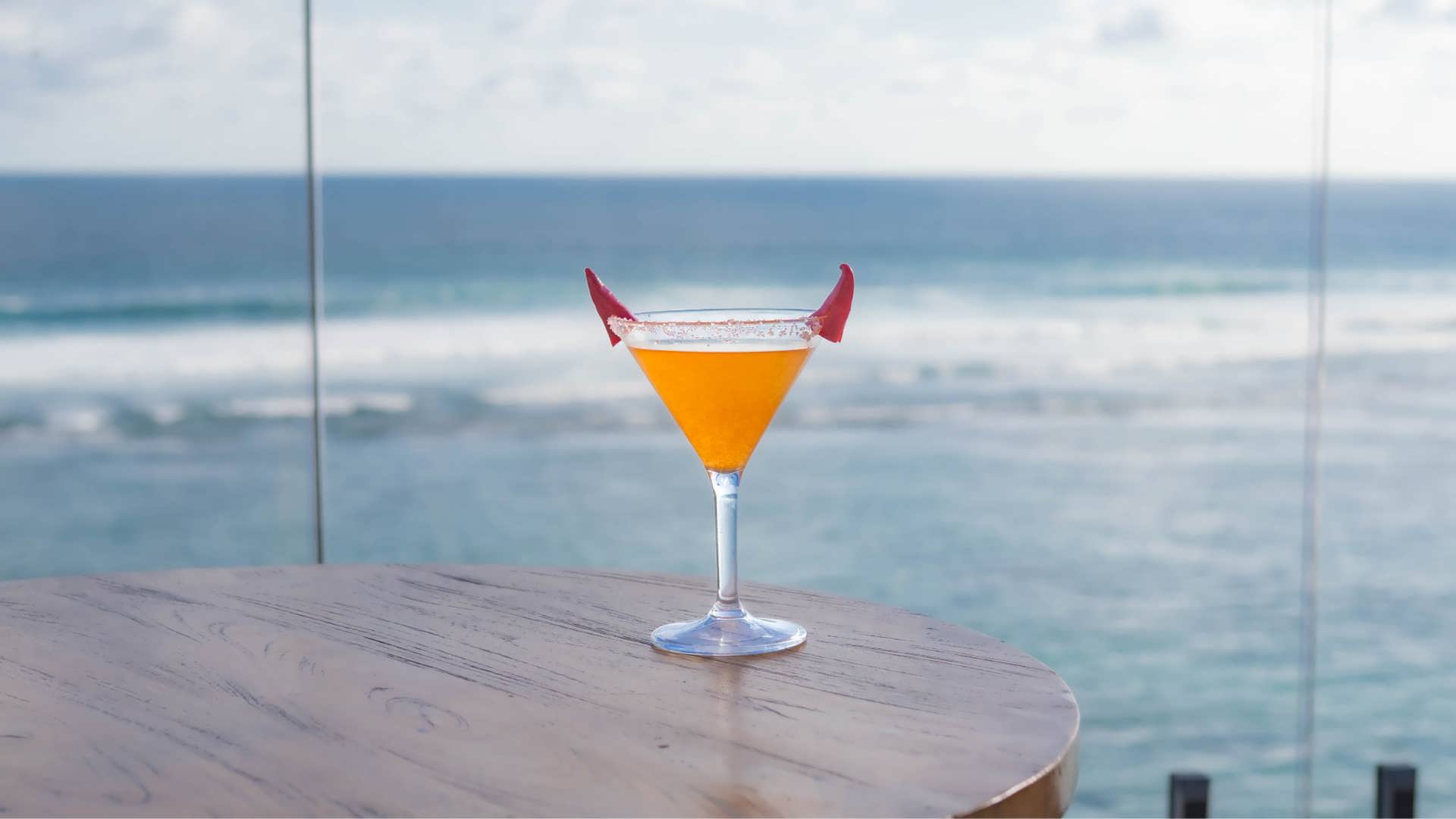Devilʼs Flame cocktail at Klive Beach Club Uluwatu — bright orange Halloween drink with red devil horn garnish overlooking the Bali ocean during Haunted by the Sea & Tropical Mischief 2025.